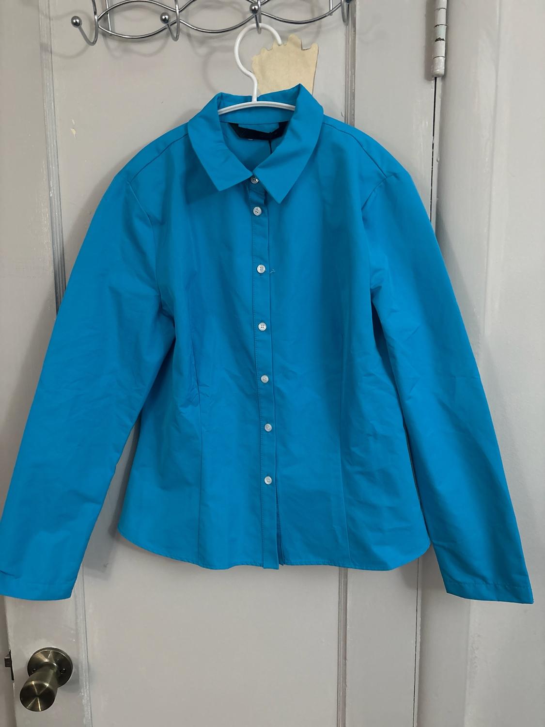 Bright blue long-sleeved button-up shirt hanging on a hanger over a white door with a metal handle.