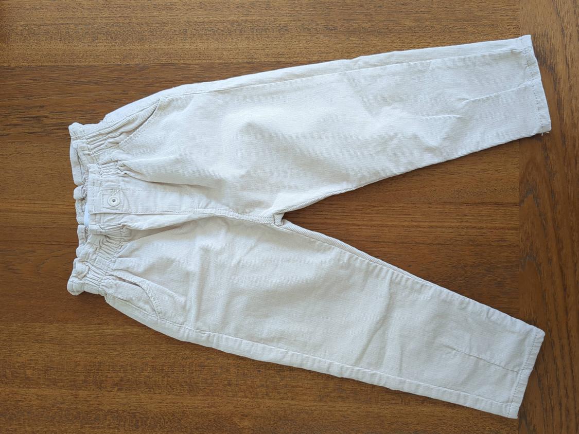 Light-colored beige pants with an elastic waist and pockets, placed on a wooden surface.