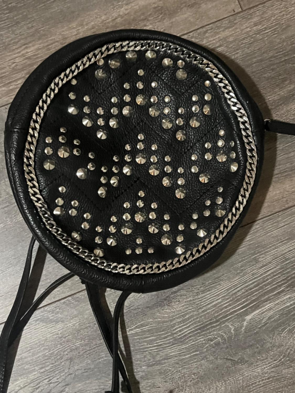 Detail of a black circular handbag with studs and a decorative metallic chain.
