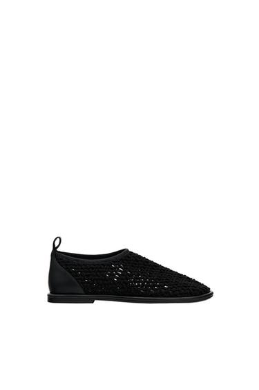 Side view of black woven footwear with a flat sole and heel detail.