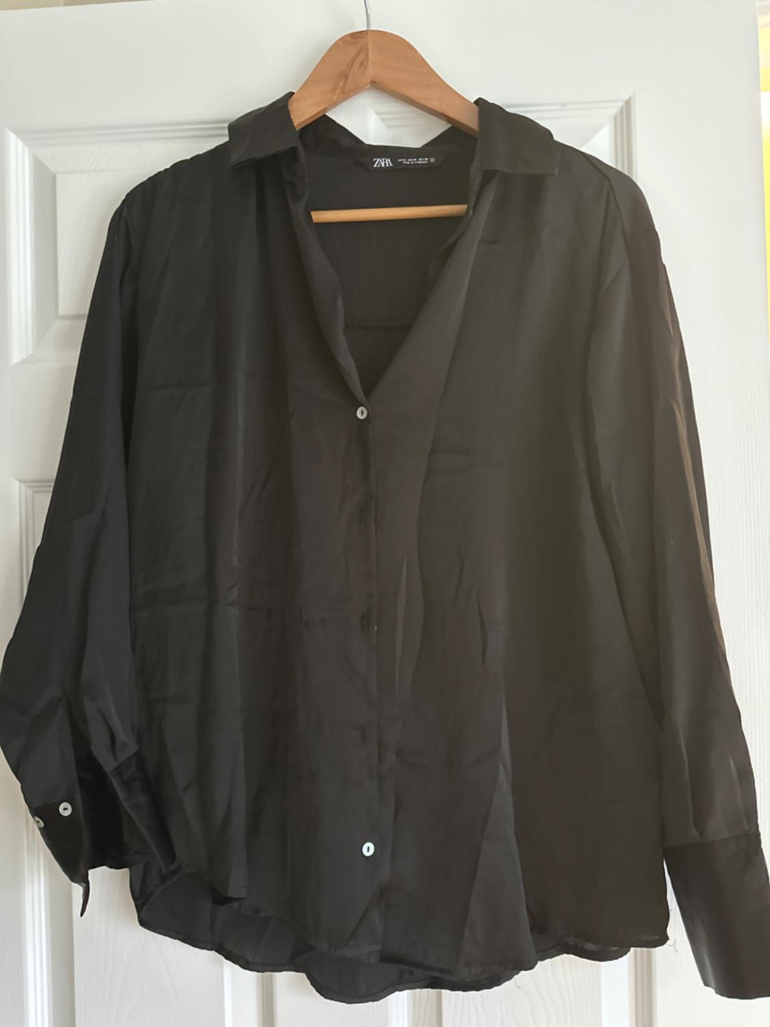 Front view of a black blouse with a collar and visible white buttons.
