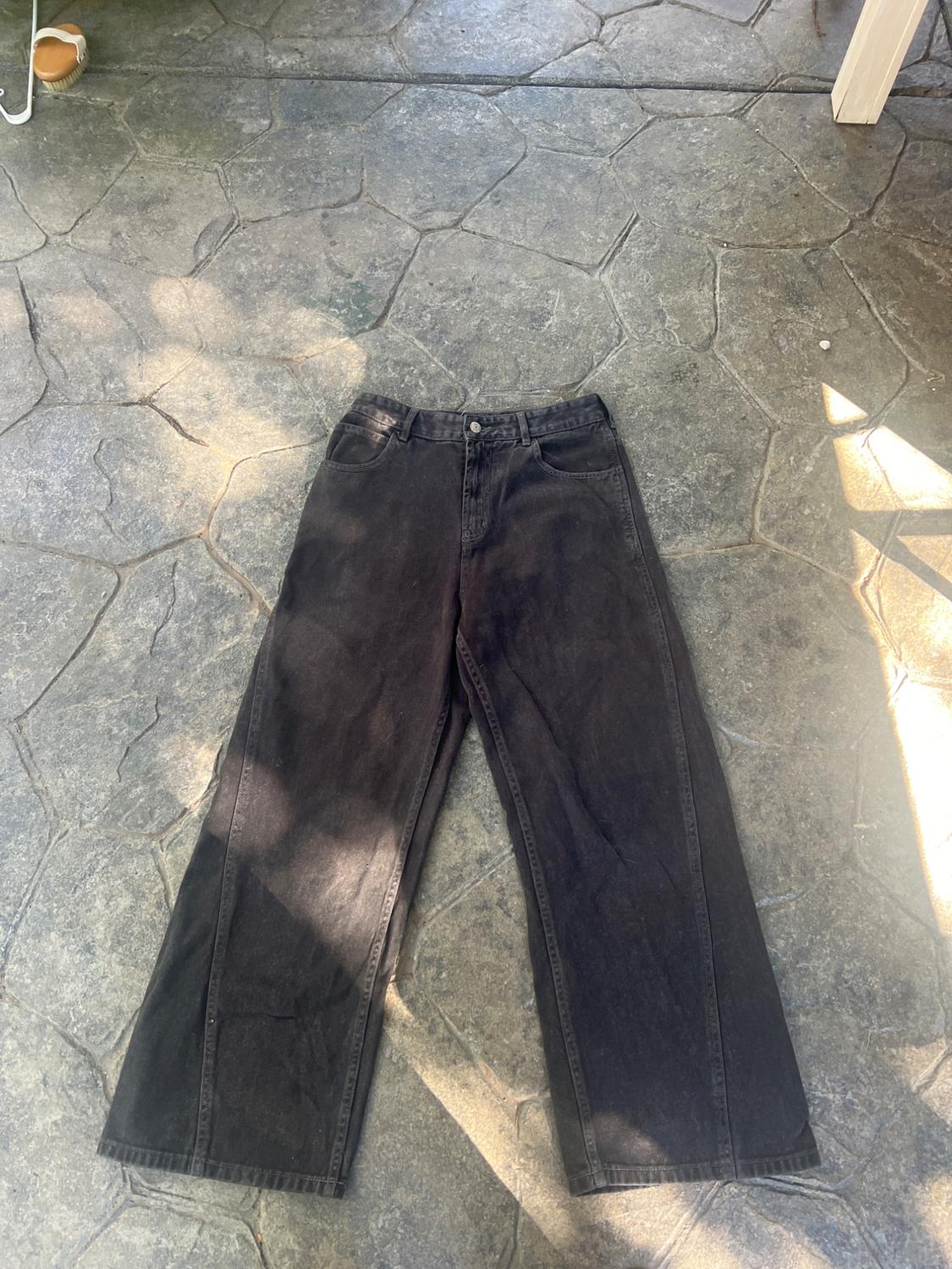 Black wide-leg jeans with front seams, on a stone floor with shadows.