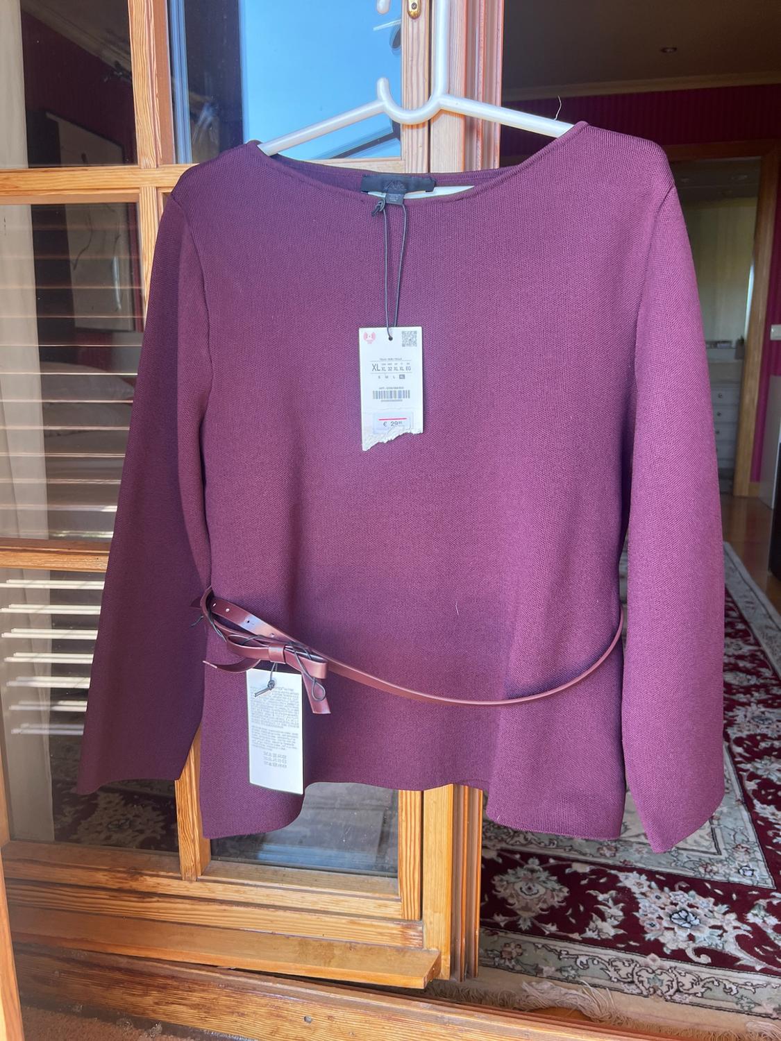 Burgundy long-sleeve knitted top on a hanger in front of a door. Includes a slim tie-belt and labels with the text XL.