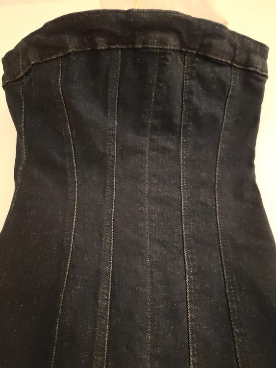 Black denim corset with visible stitching, viewed from the back. Fabric with a slight sheen under warm light.