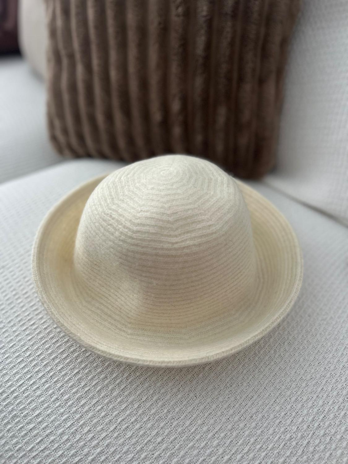 Beige hat on a white textured sofa, with a brown cushion in the background. Relaxed and cosy atmosphere.