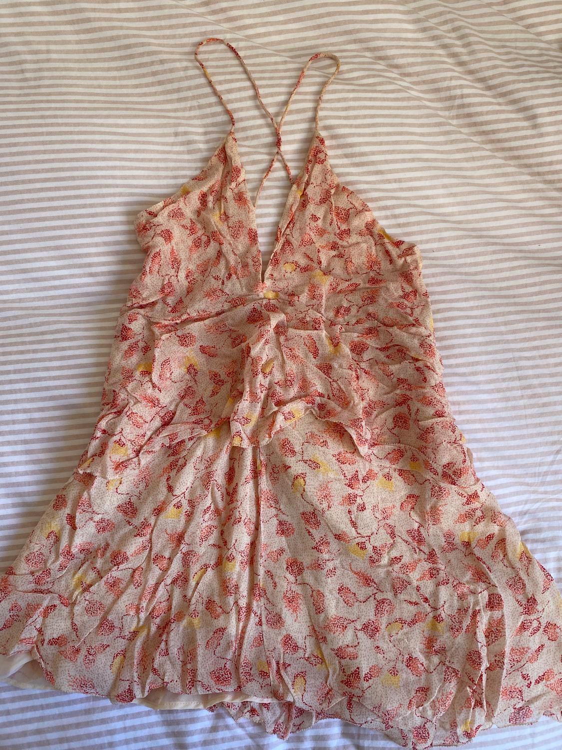 Red and yellow floral print camisole dress on a beige background, placed on a white and beige striped fabric.