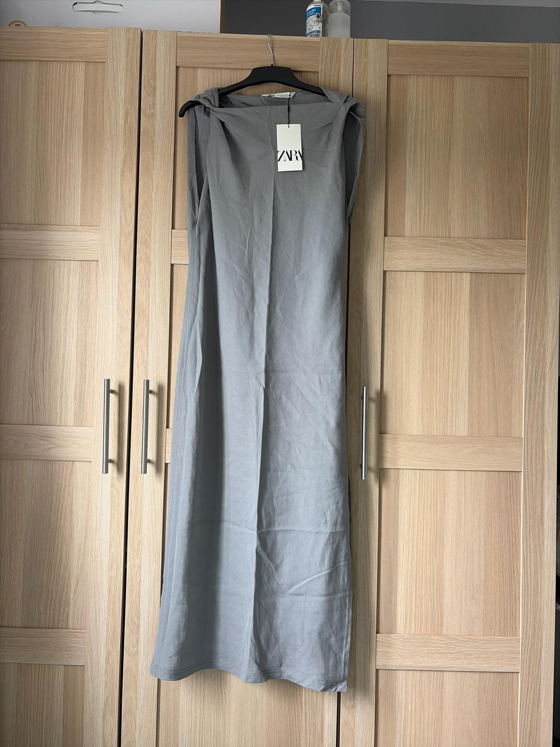 Grey sleeveless maxi dress hanging in a wooden wardrobe. Label with the text ZARA. Casual style and relaxed home atmosphere.