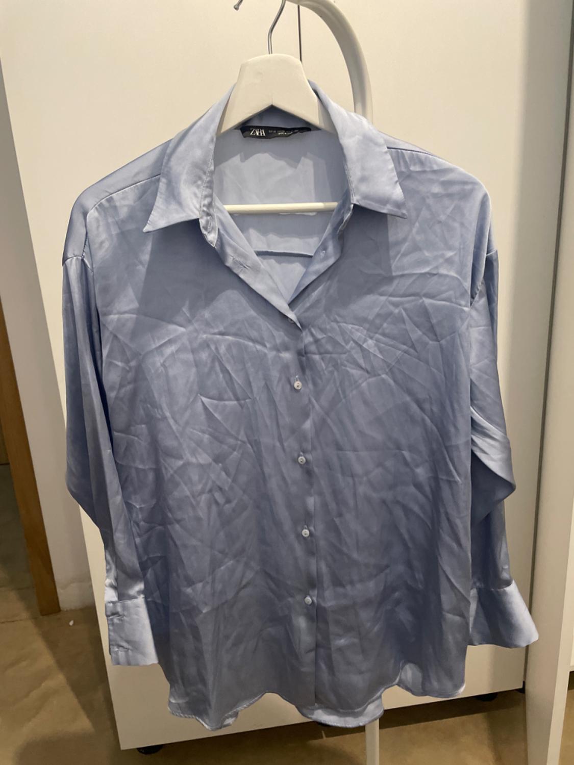 Light blue crumpled shirt hanging on a white hanger inside a wardrobe. White background and beige floor visible.