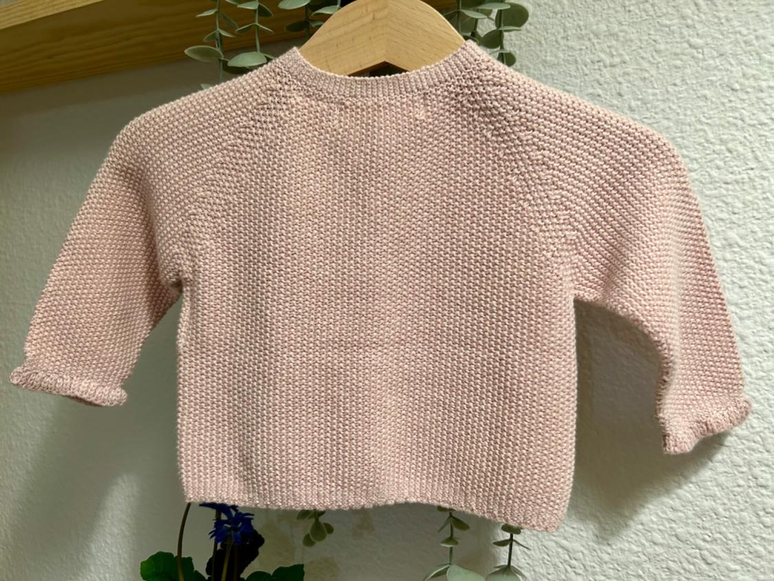 Back view of a light pink knitted textured sweater with long sleeves.
