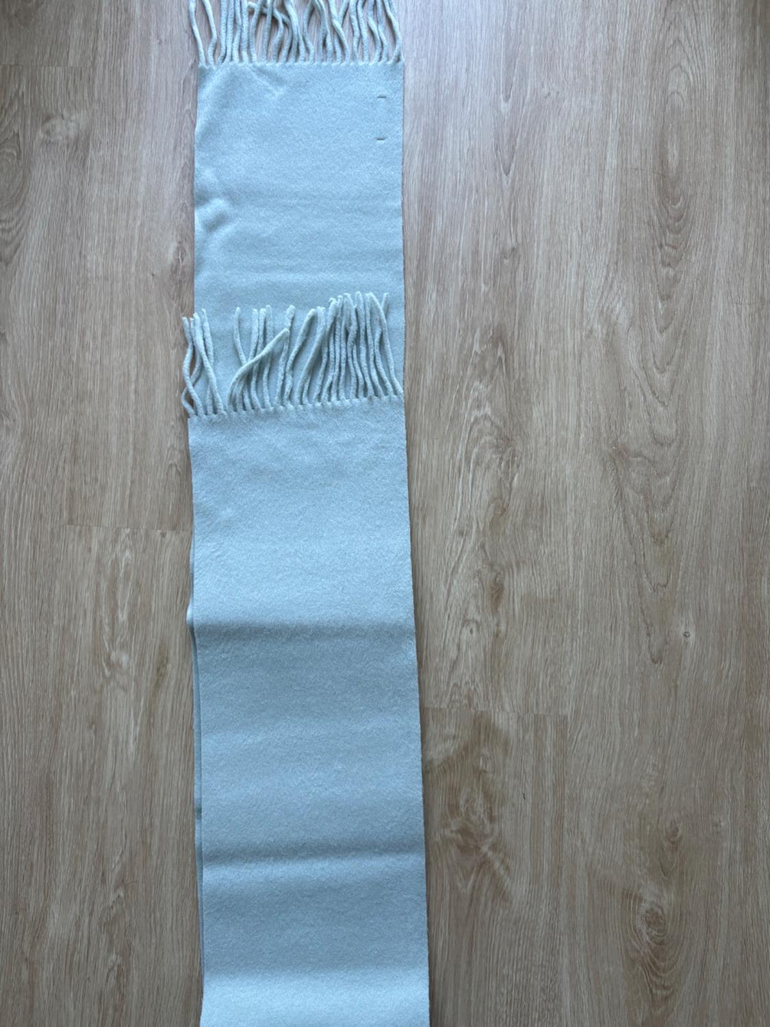 Light blue fringed scarf, folded and laid out vertically on a wooden floor.