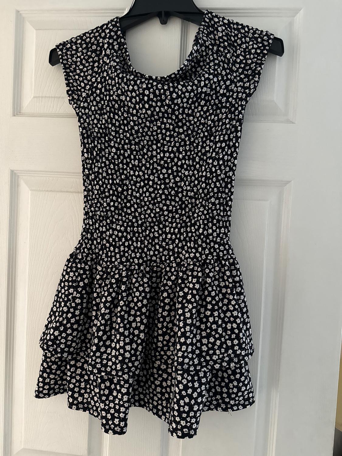 Black dress with small white floral print, sleeveless, hanging on a white door.