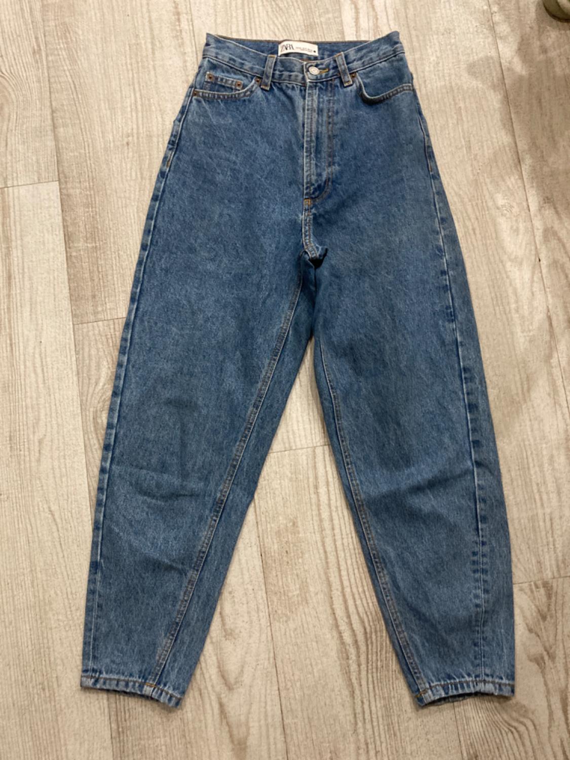 High-waisted, straight-cut blue jeans, placed on a light wooden floor. Label visible on the inside.
