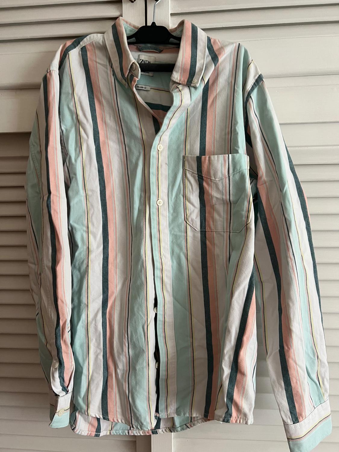 A pastel-coloured vertical striped shirt hanging on a black hanger in front of a white door background.