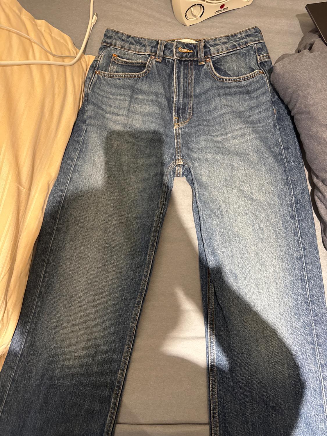 Blue denim jeans on a bed, surrounded by yellow and grey sheets. There is a shadow cast over them.