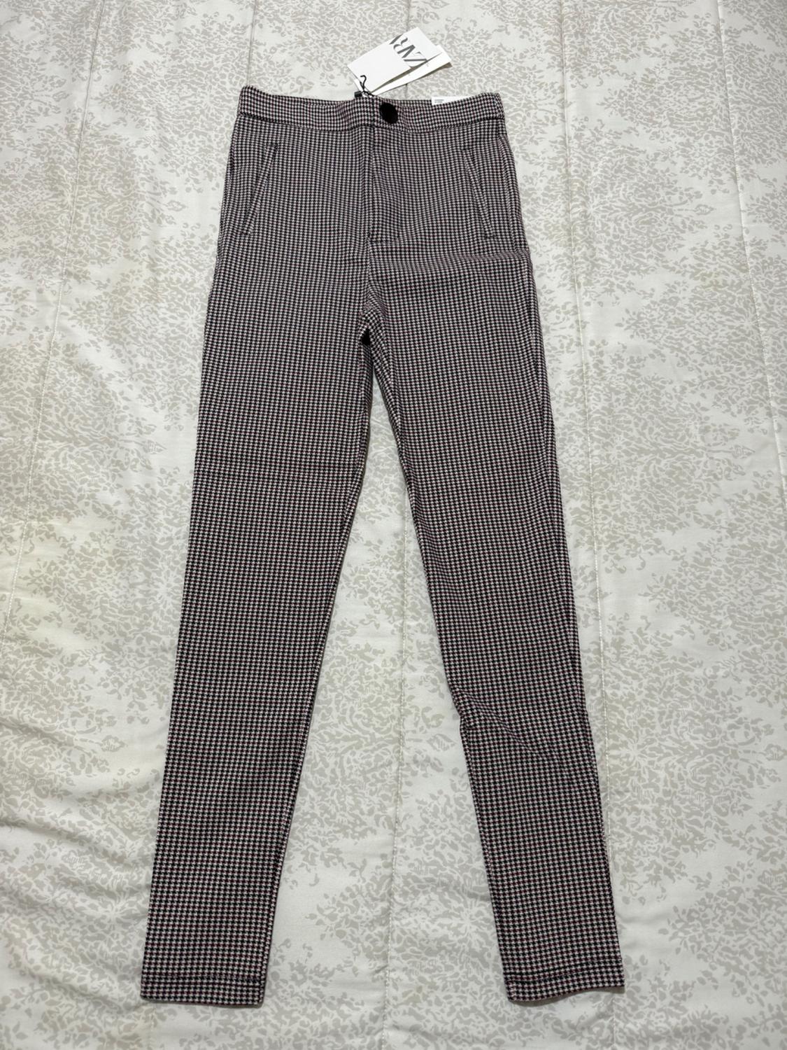 Small black and white check trousers on a patterned surface. Visible label with the text "ZARA".