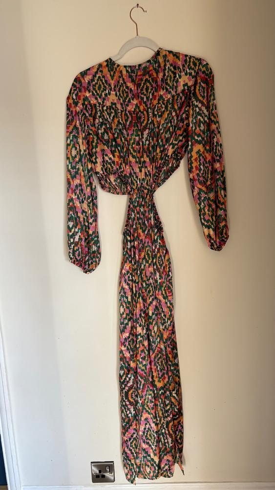 Long dress hanging on a hanger, with a geometric print in shades of green, pink, and orange, and long puff sleeves.