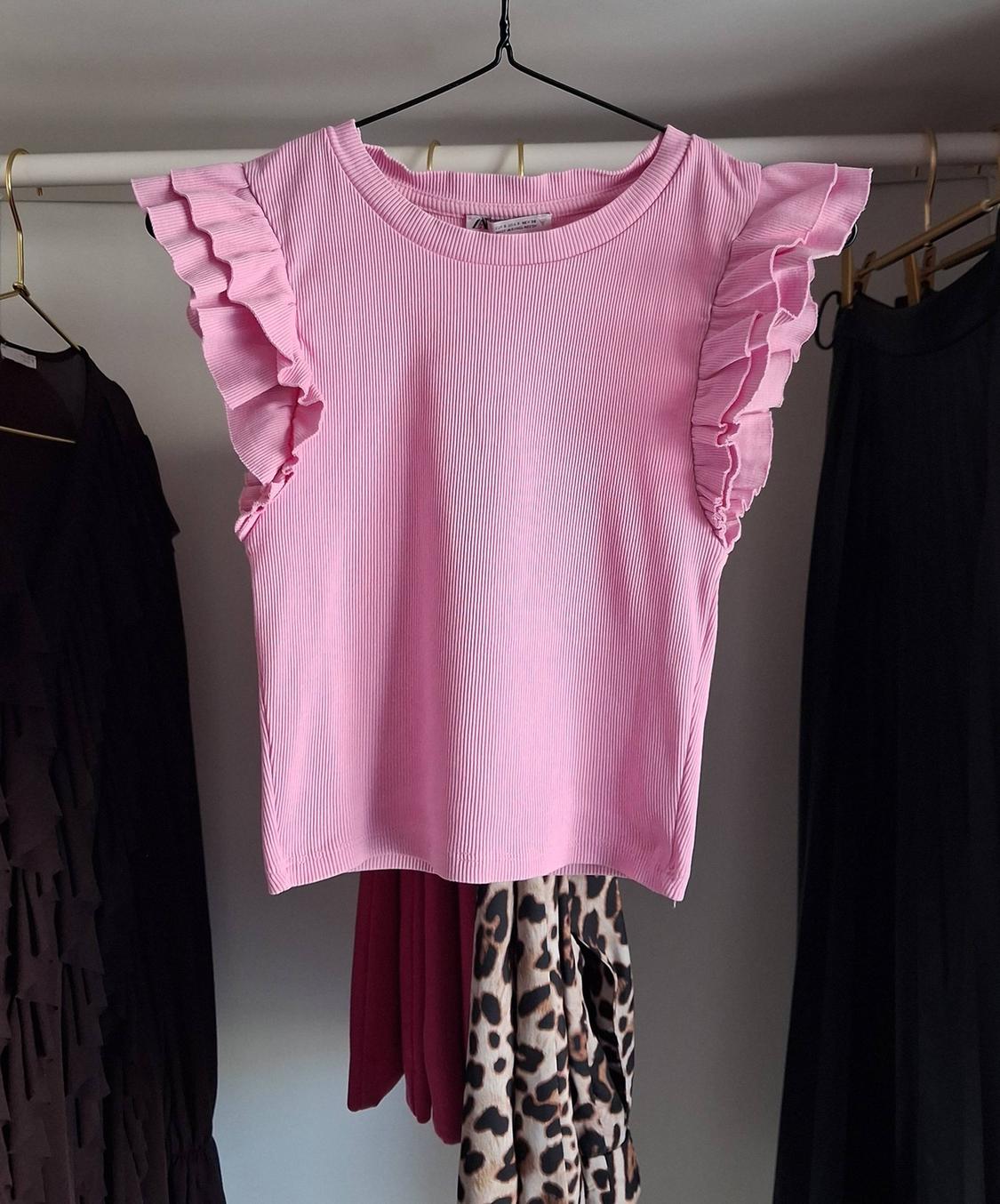 Pink blouse with ruffled sleeves hanging on a clothes rail, surrounded by dark garments and animal print.