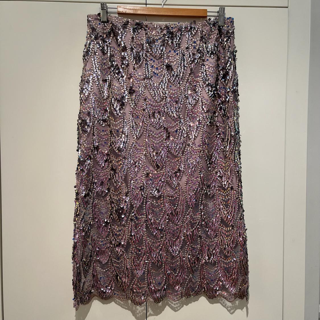 Purple and silver sequin skirt with a wavy design and scalloped hem. It is hanging on a hanger in front of a white wardrobe.