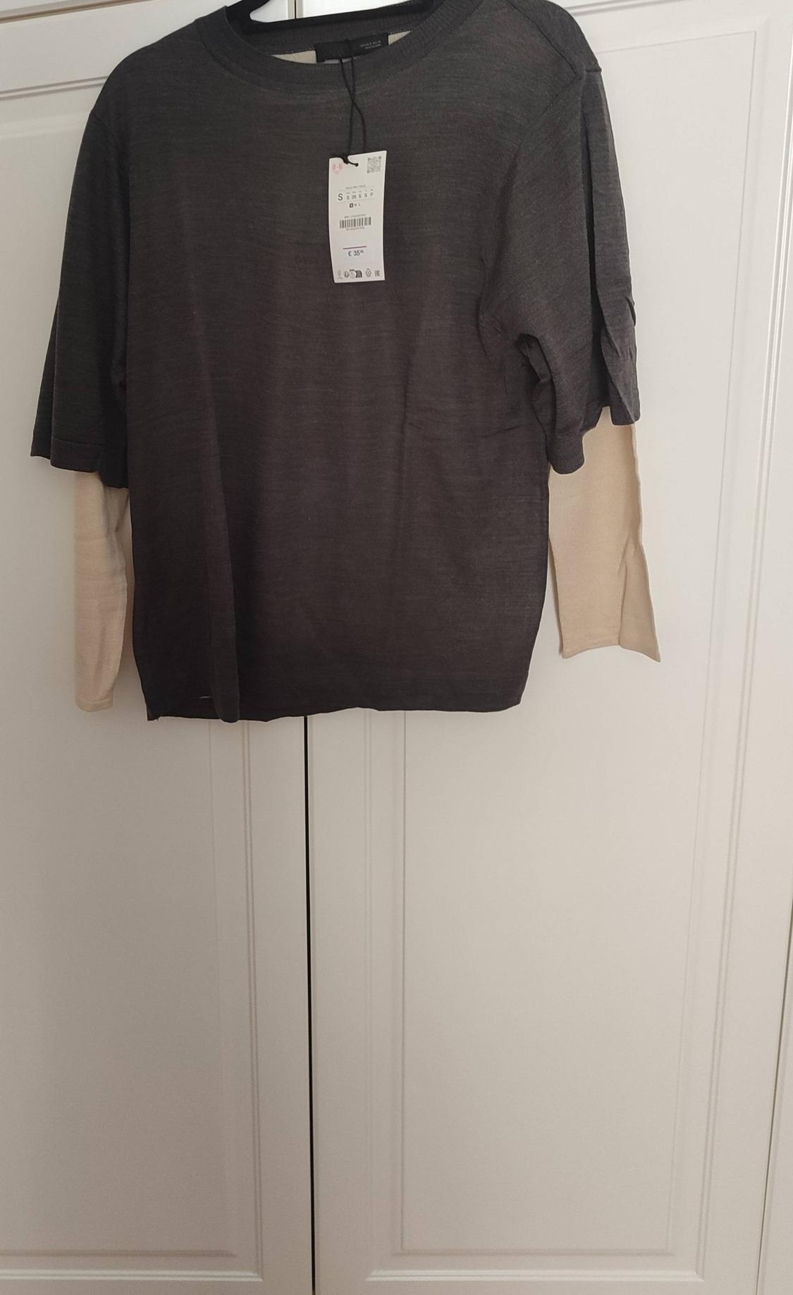Grey short-sleeved T-shirt hanging on a white door, with price tag visible in the centre.