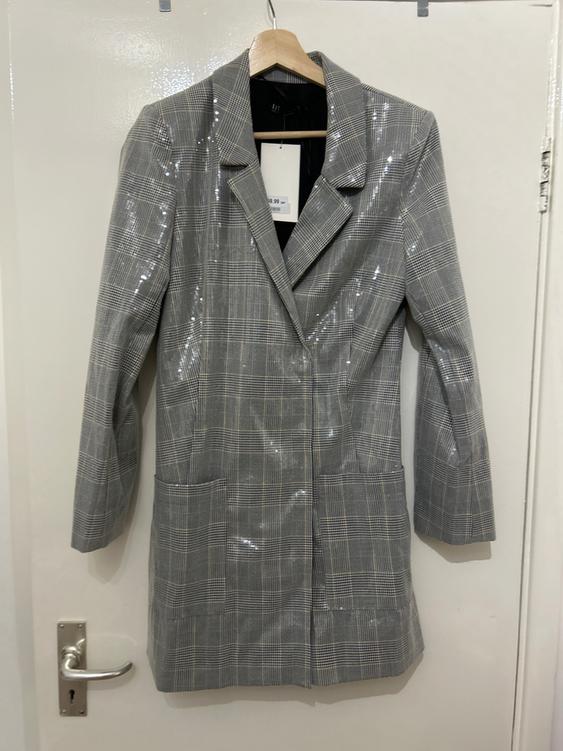 Grey coat with a plaid pattern, hanging on a wooden hanger over a white door. Label visible on the collar.