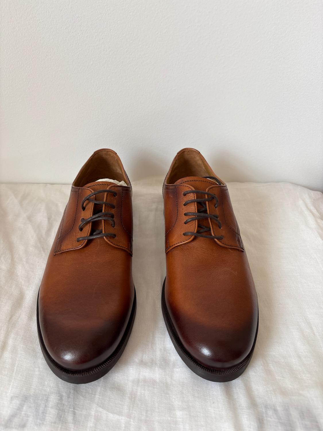 Brown leather shoes with black laces on a white cloth. Plain white background.