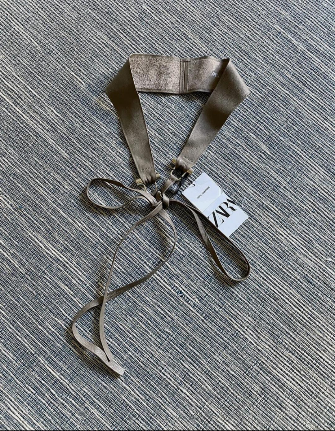 Brown belt with bow on a textured grey rug. Visible label with the text "ZARA".