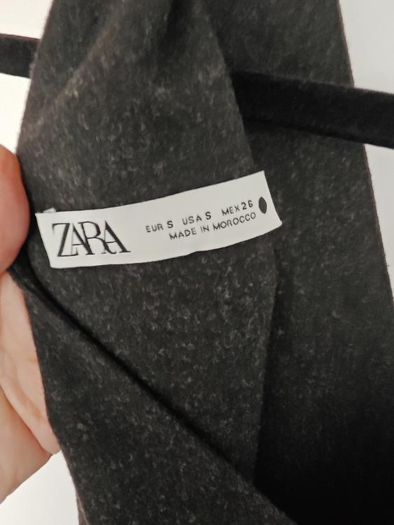Zara clothing label on dark grey fabric, showing sizes EUR S, USA S, MEX 26, made in Morocco.