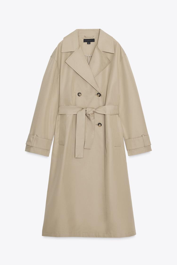 Front view of a long, tan trench coat with a lapel collar, long sleeves, jetted front pockets, and a matching belt.