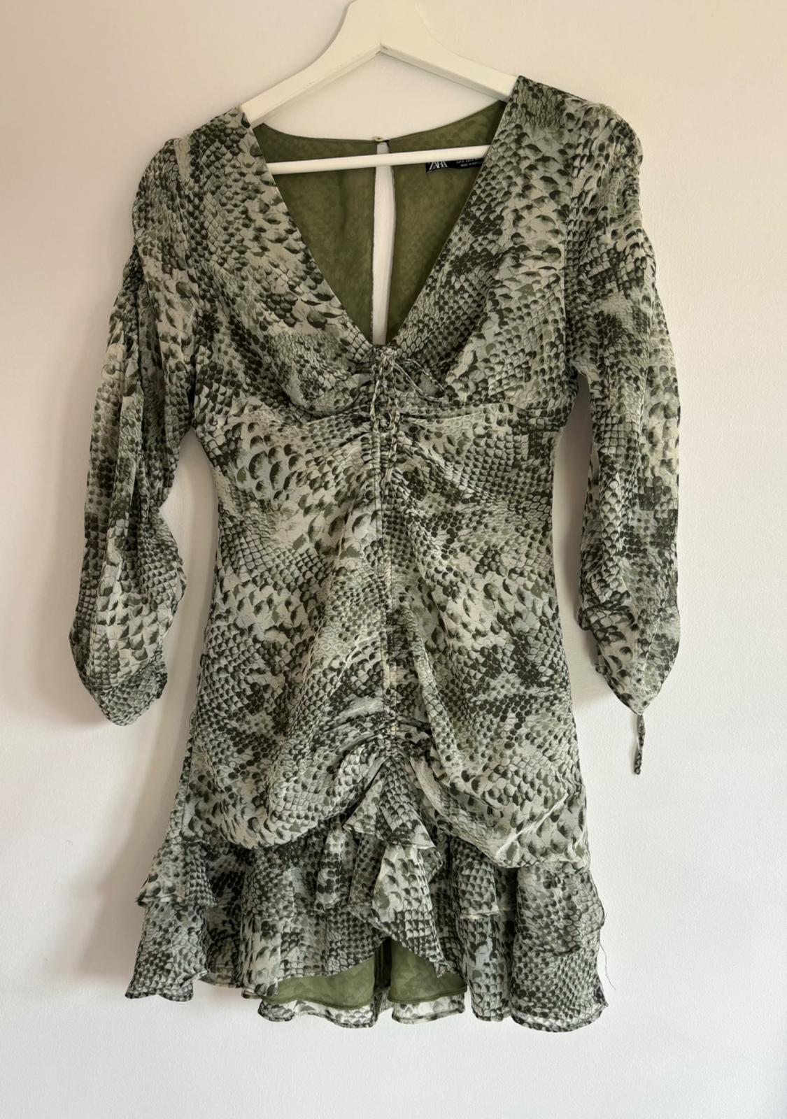 Κοντό φόρεμα με πράσινο snake print, μακρύ μανίκι με βολάν και V ντεκολτέ, κρεμασμένο σε μια λευκή κρεμάστρα.