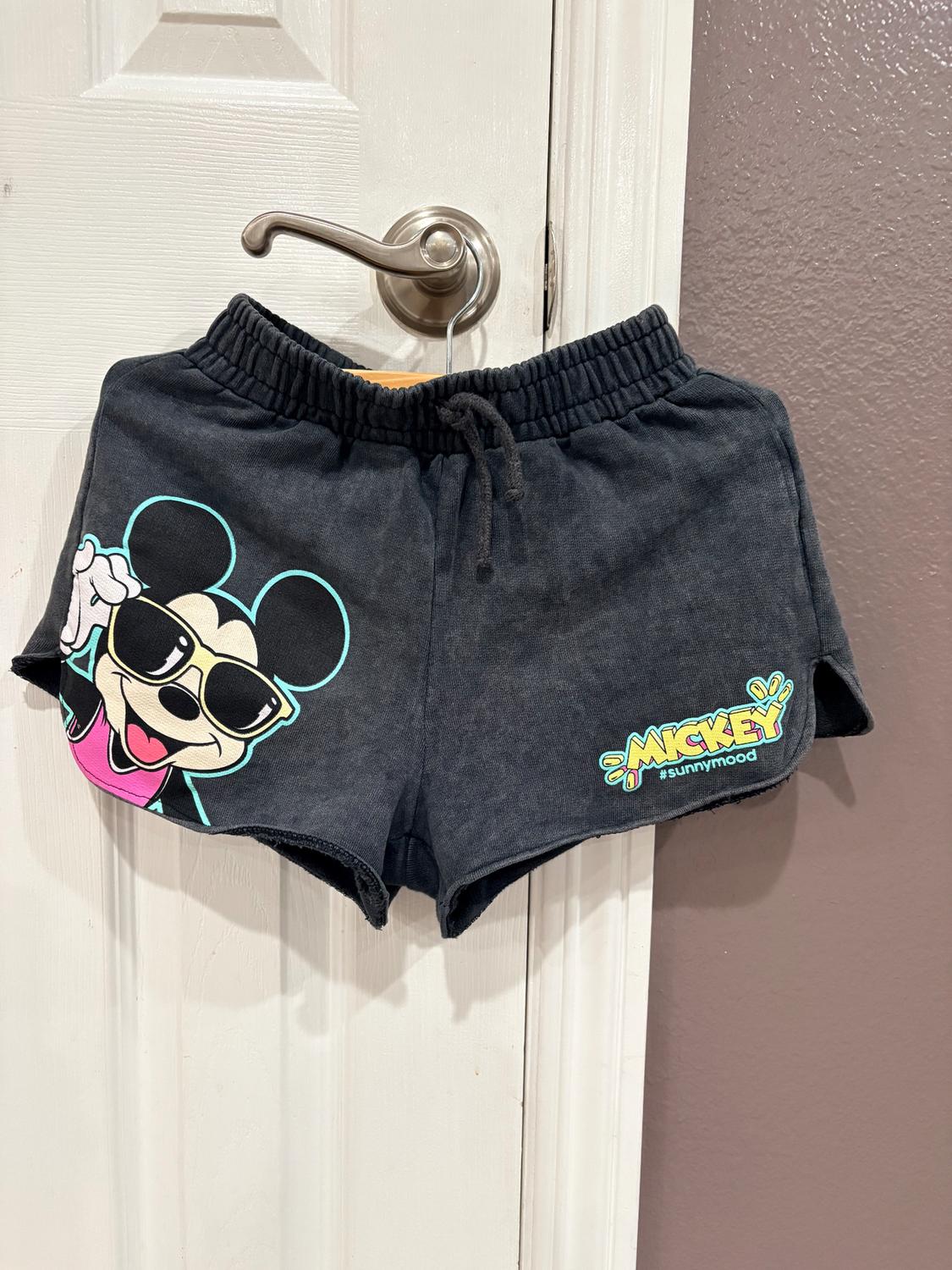 Black shorts hanging on a door, with a drawing of a mouse wearing sunglasses and the text "Mickey #sunnymood" in bright colors.