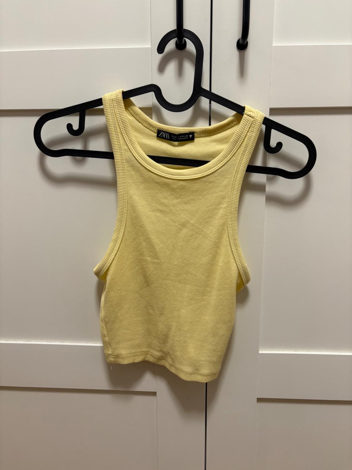 Yellow ribbed cropped top hanging on a black hanger in front of a white wardrobe. Label with the text ZARA.