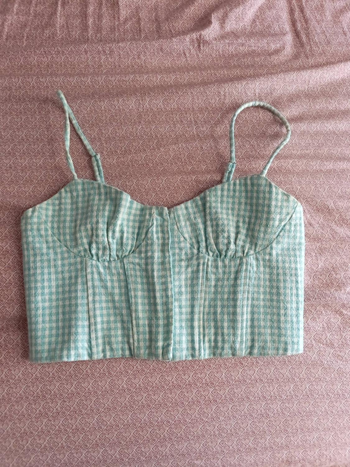 Bustier-style top with thin straps in a light blue and white checked pattern on a pink fabric background.