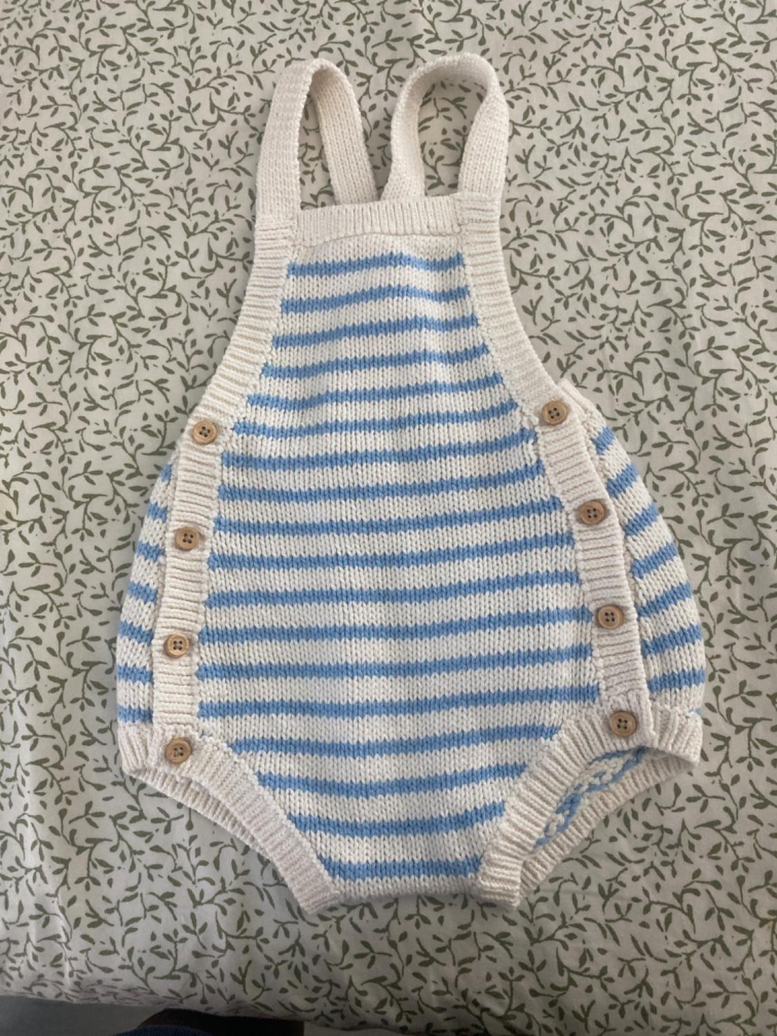 Knitted romper with blue and white stripes and wooden buttons, on fabric with a green leaf pattern.