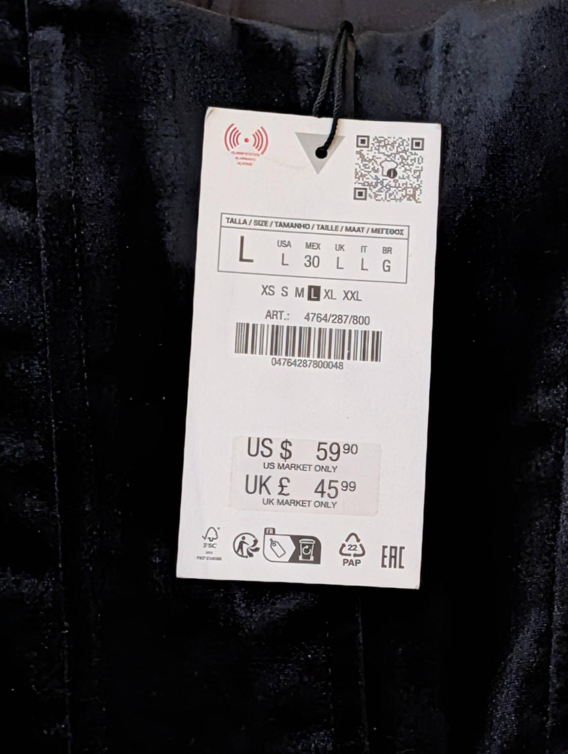 Clothing tag on black fabric, showing sizes L, price US $59.90, UK £45.99, and barcode. Text: "US MARKET ONLY", "UK MARKET ONLY".