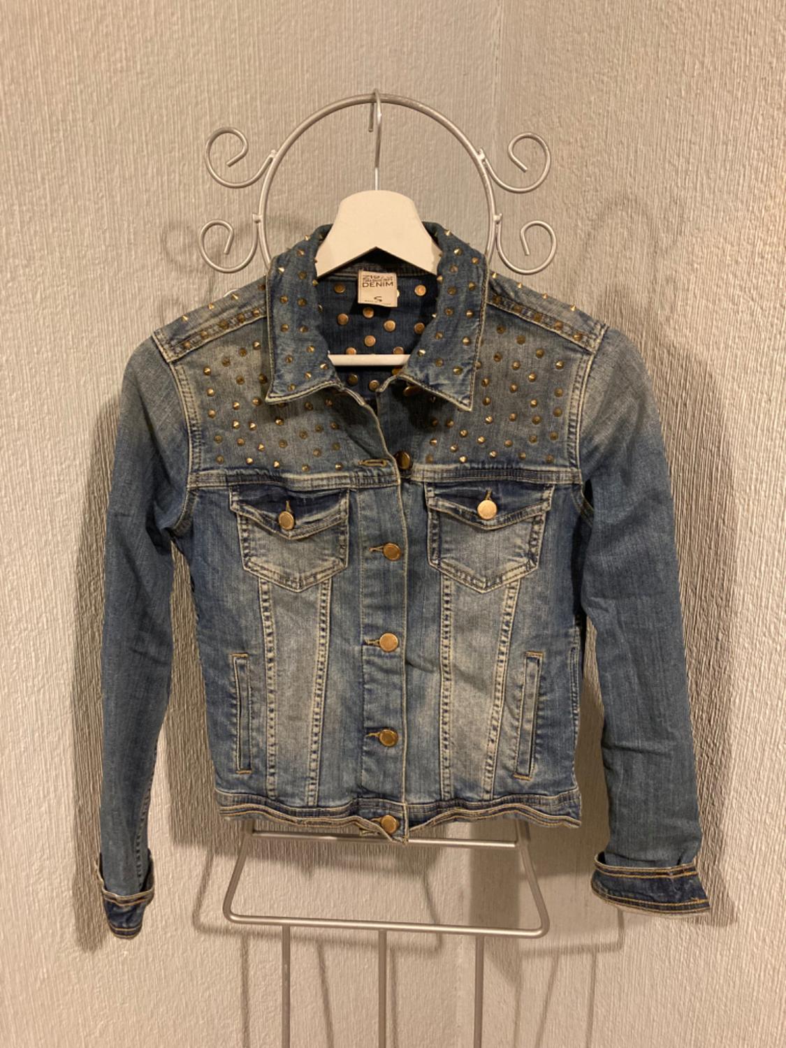 Front view of a blue denim jacket with gold studs and front flap pockets.