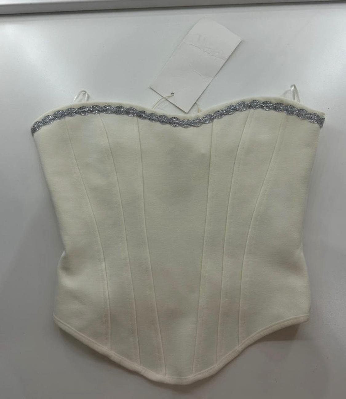 White strapless corset-style top with silver trim on the neckline and vertical seams, on a white surface with a label.