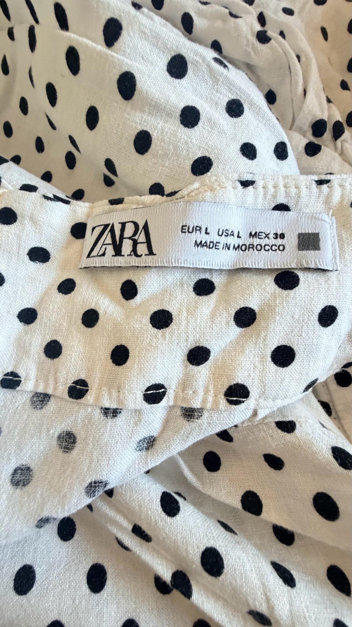 Detail of white fabric with black polka dots and a label with the text ZARA EUR L USA L MEX 30 MADE IN MOROCCO.