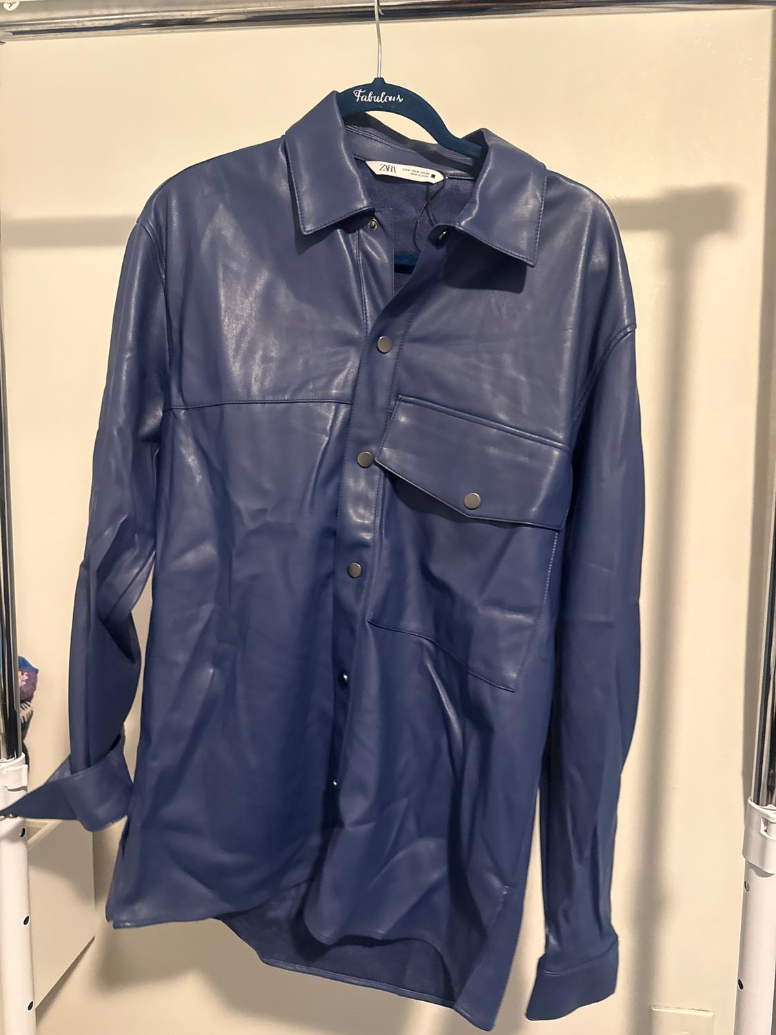 Blue synthetic shirt hanging on a blue hanger with the brand "Fabulous". It has front pockets and metal buttons.