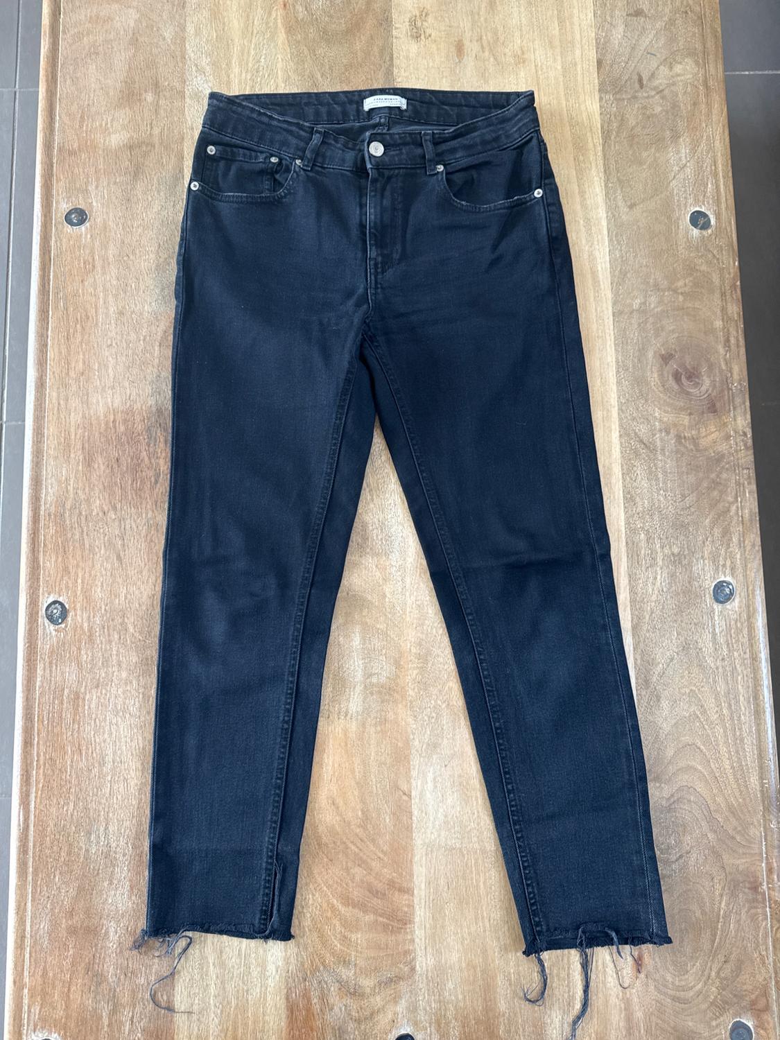 Front view of black denim jeans with front pockets and frayed hems.