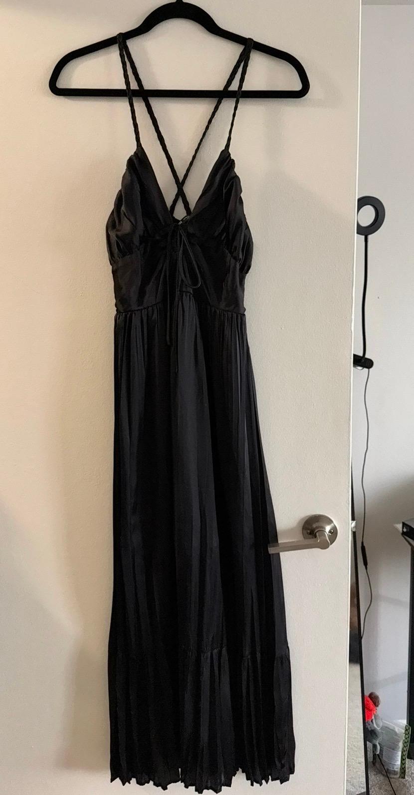 Long black dress with criss-cross straps, hanging on a black hanger over a white door. Minimalist indoor setting.