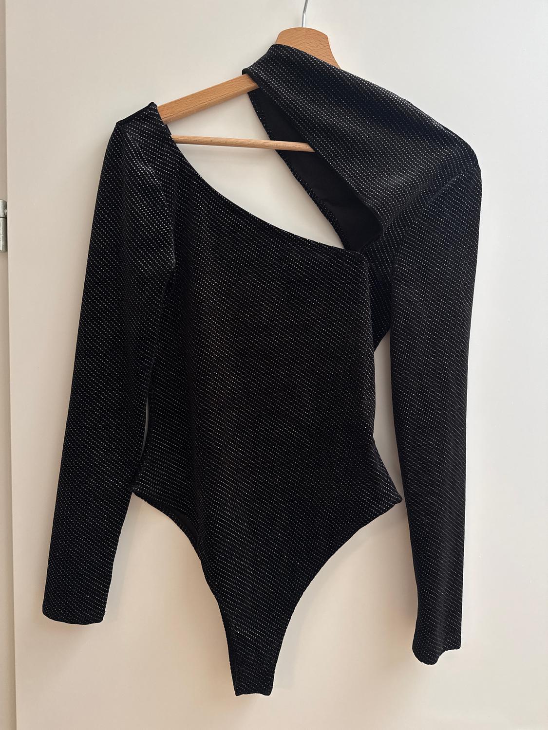Black long-sleeved bodysuit with an asymmetrical design and shiny texture, hanging on a wooden hanger against a white background.