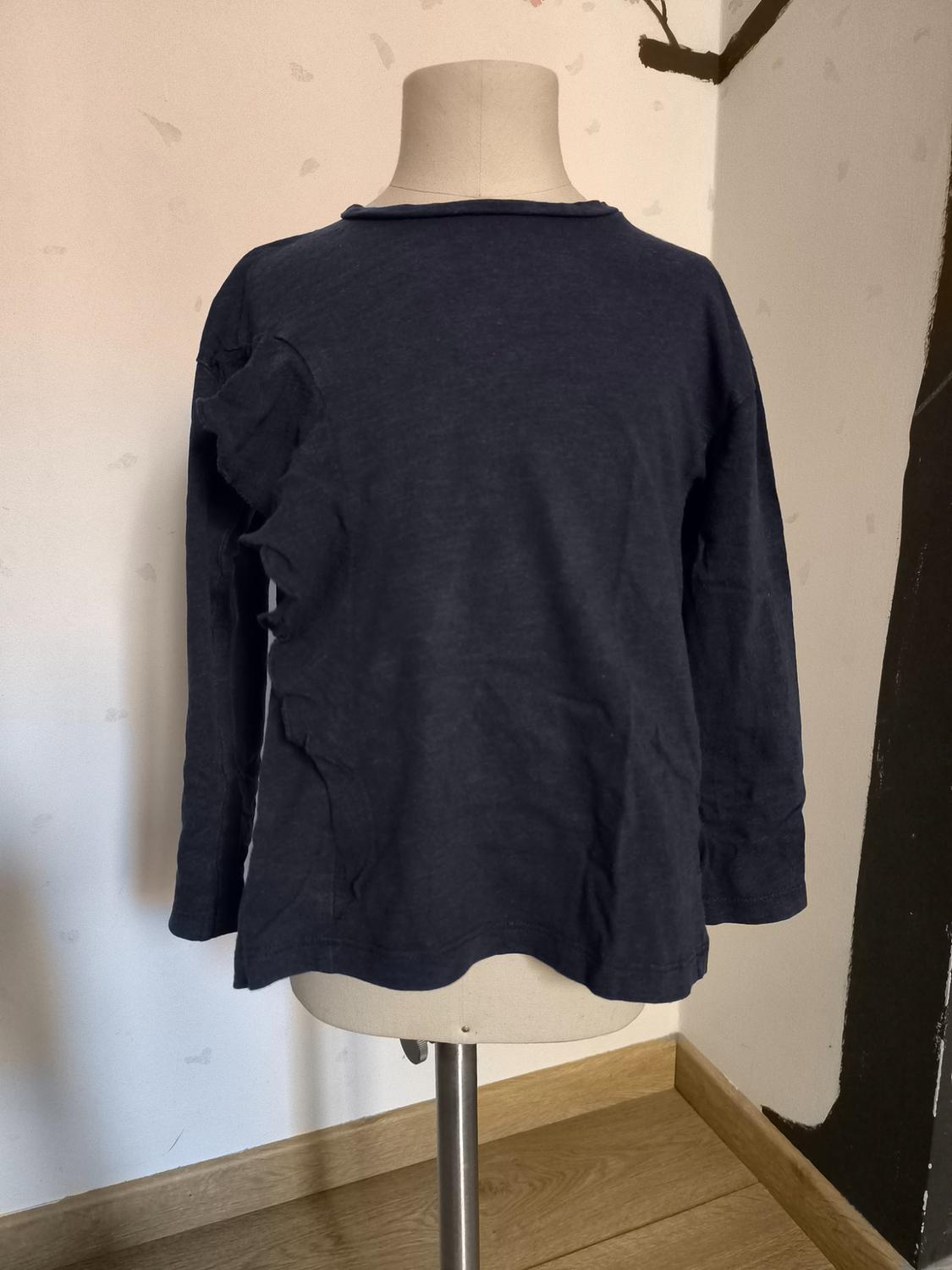 Μανεκέν με σκούρο μπλε μακρυμάνικο T-shirt σε γωνία δωματίου με ανοιχτόχρωμους τοίχους και ξύλινο πάτωμα.