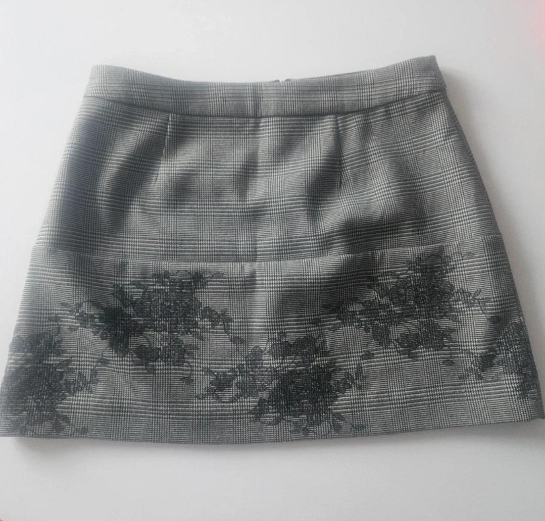 Grey mini skirt with a checked print and black flowers at the bottom, on a white background.
