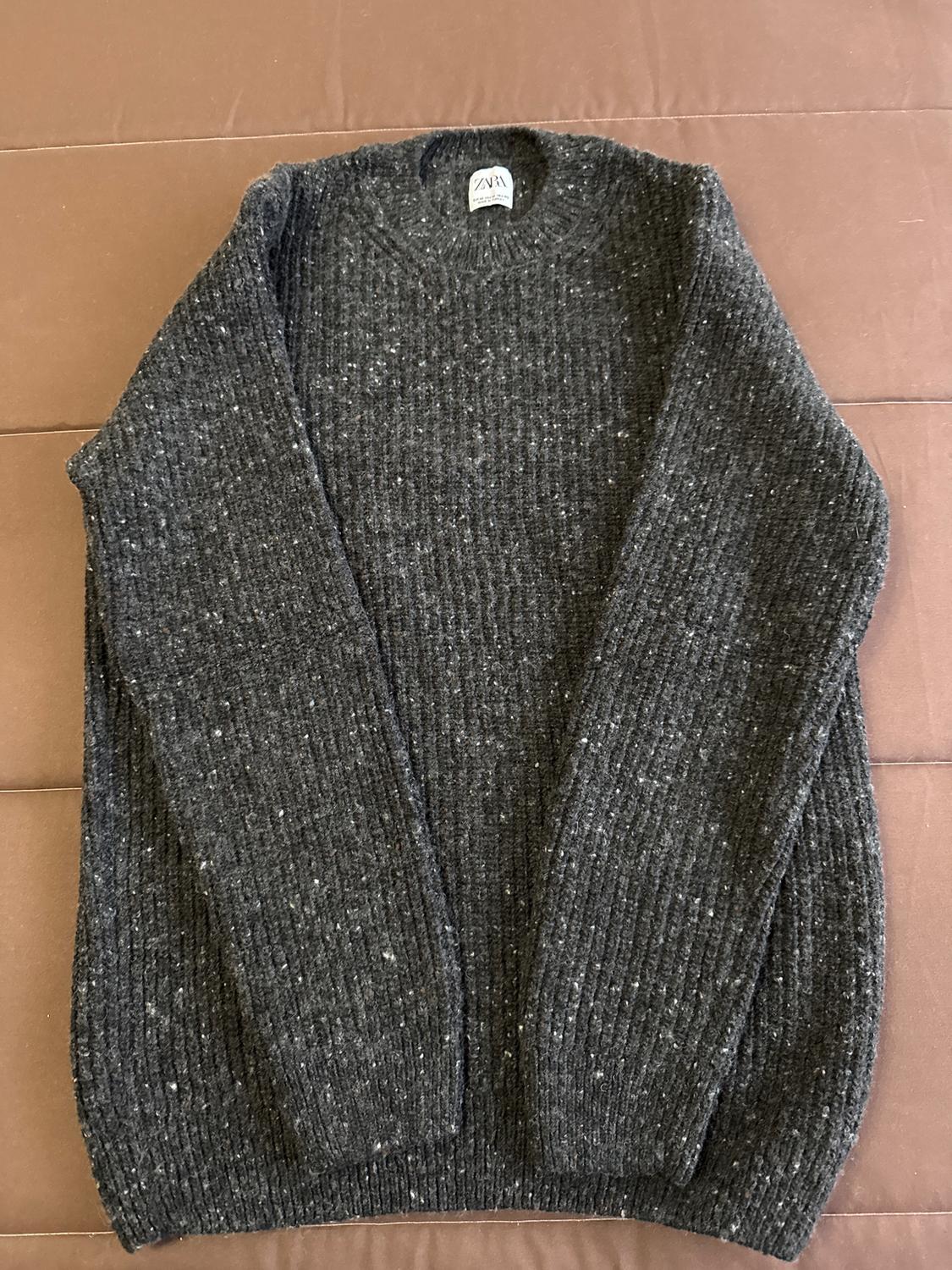 Dark grey chunky knit jumper with a speckled texture, placed on a brown surface. Visible label on the collar.