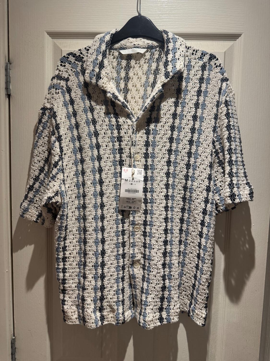 Knitted shirt hung on a black hanger, with a blue and white striped pattern, and visible label in the centre.