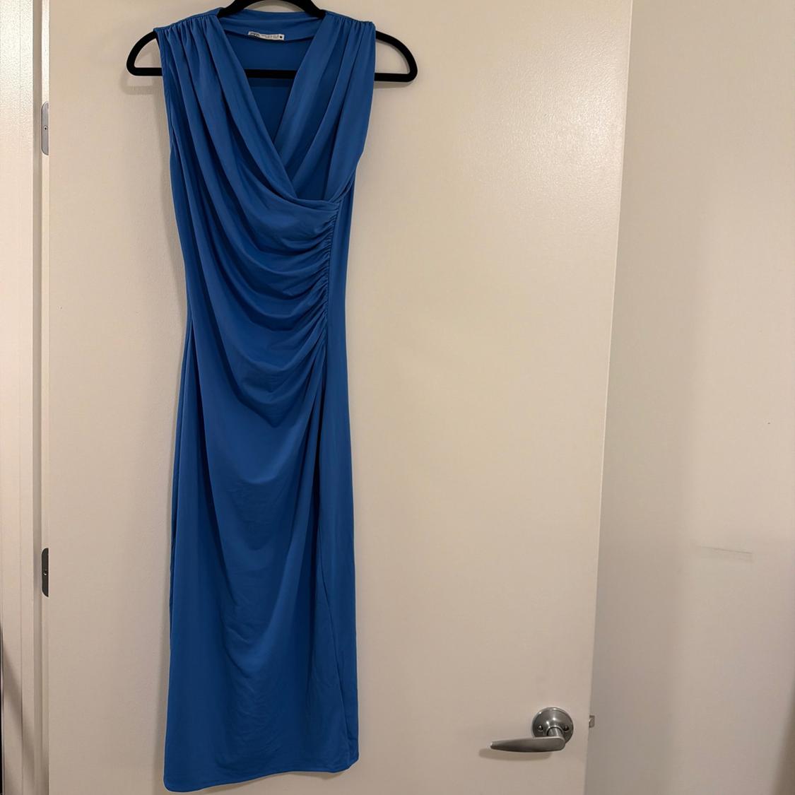 Blue sleeveless dress with draped detail, hanging on a black hanger on a white door.