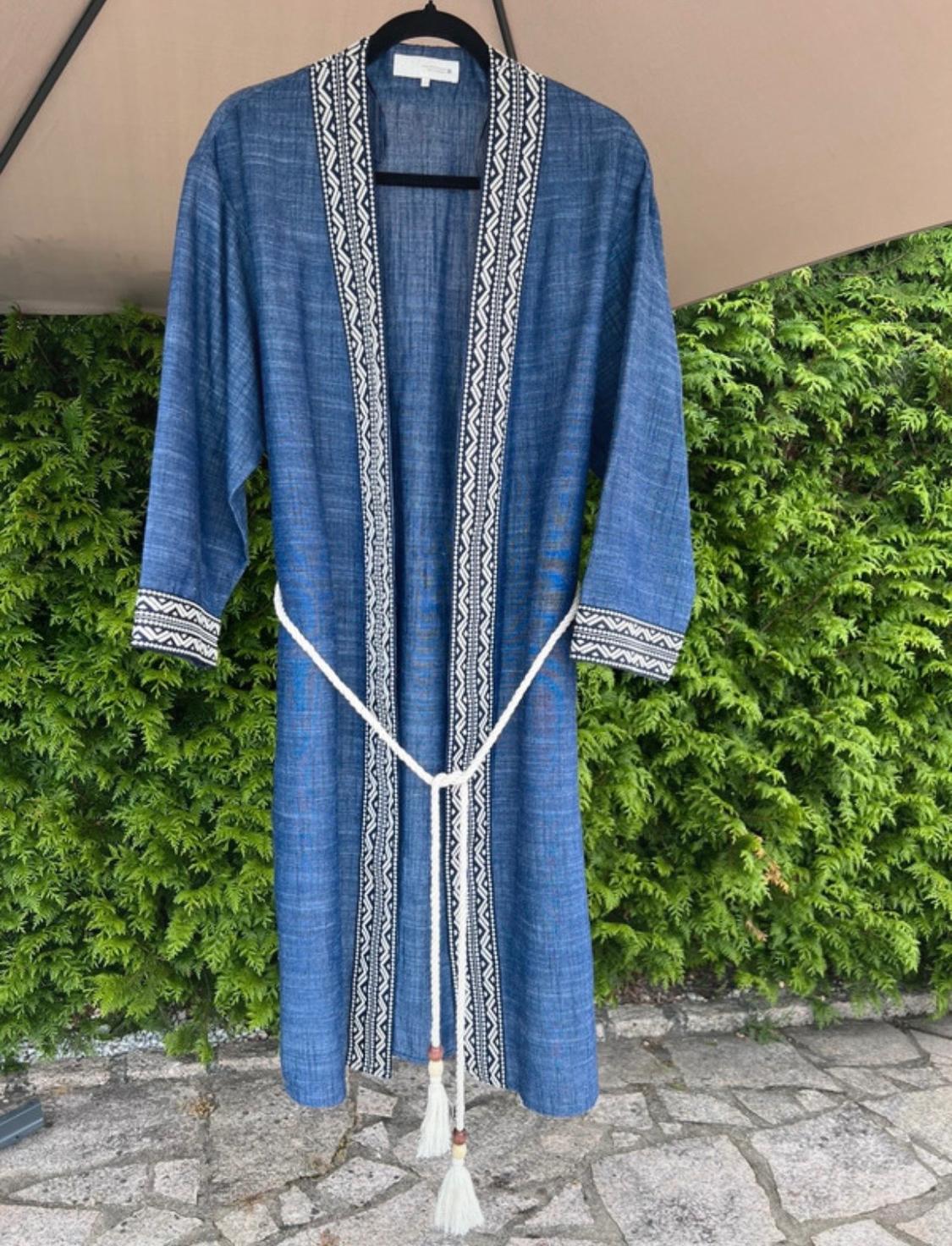 Blue kimono hanging outdoors. Notable for its black and white geometric patterned trim and a rope belt with tassels.
