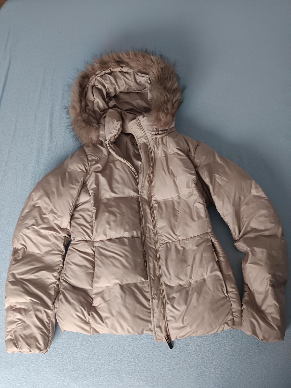 Beige padded jacket with a faux fur hood on a blue surface. The zip is partially open.