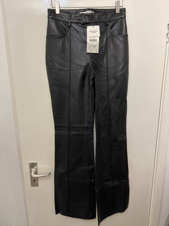 Black leather trousers hanging on a white door, with a tag that says "Genuine Leather Garment" and a price of 149.