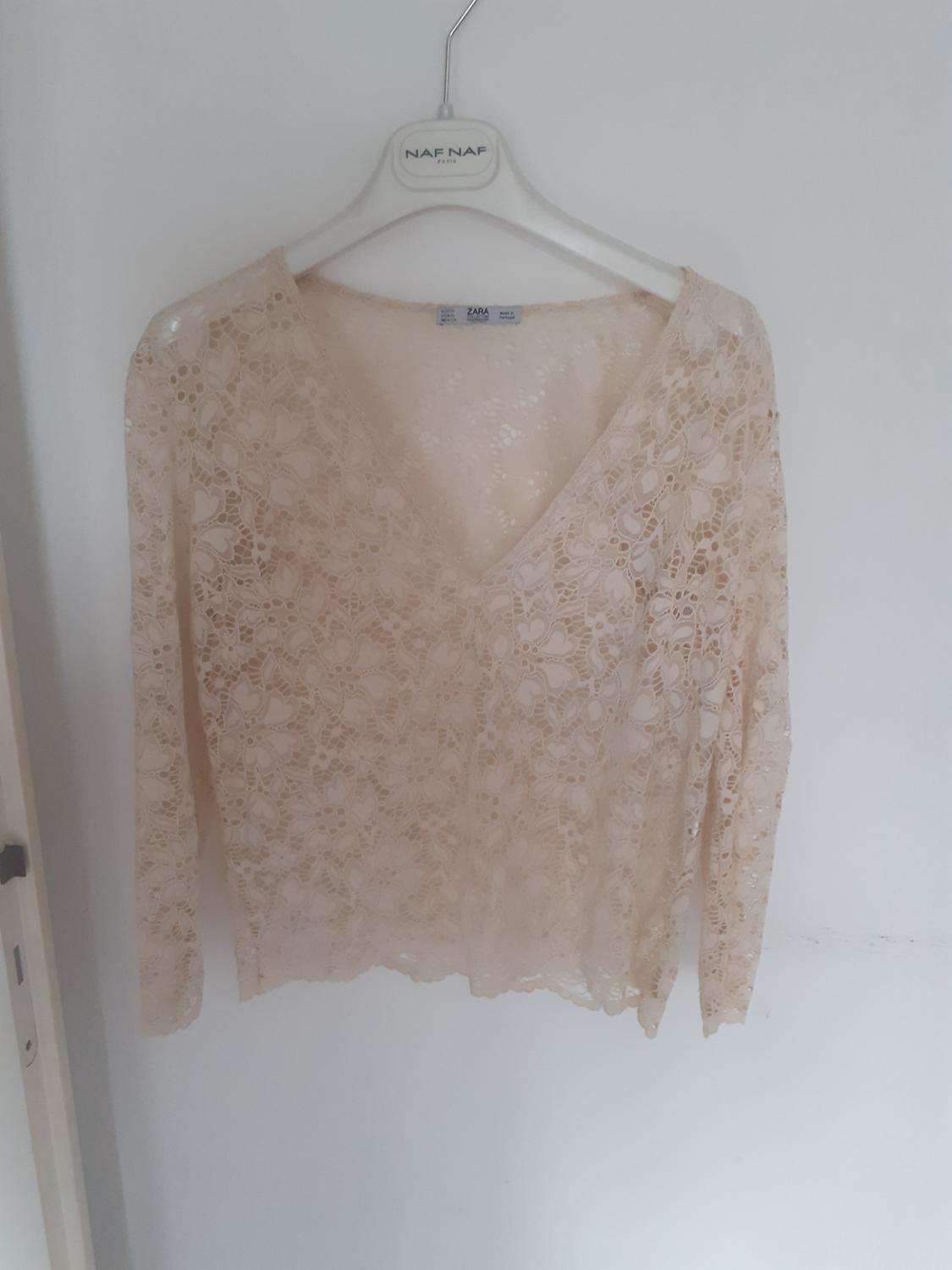 Beige long-sleeved lace top with a V-neck hanging on a white hanger. Visible text: NAF NAF PARIS, ZARA.